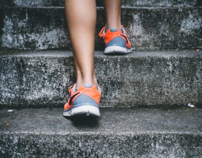 person wearing orange and gray Nike shoes walking on gray concrete stairs