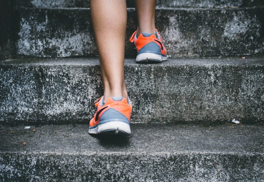 person wearing orange and gray Nike shoes walking on gray concrete stairs