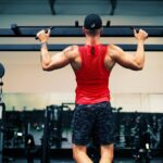 man in red tank top and black shorts holding black dumbbell