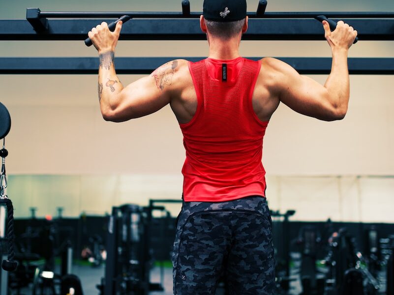 man in red tank top and black shorts holding black dumbbell