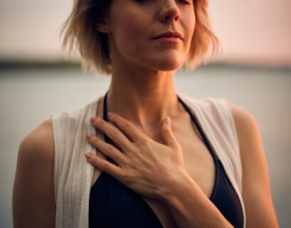 woman in white vest and black bikini with hand on chest