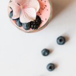 pink beverage on glass with blackberries and pink flower on top